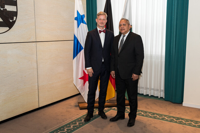 Zwei Männer stehen vor einer Fahnengalerie.