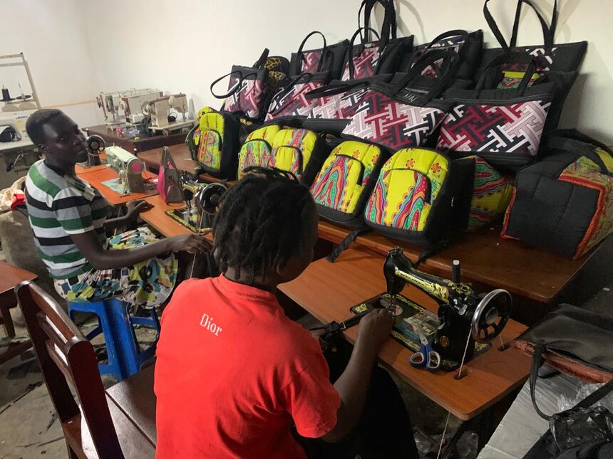 Zwei Personen arbeiten an Nähmaschinen und stellen Taschen und Rucksäcke her.