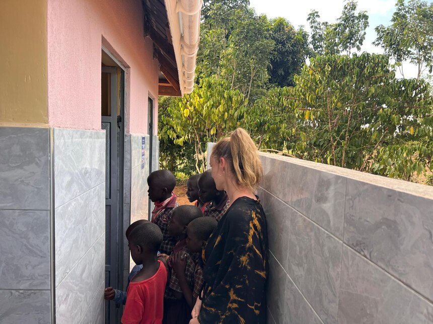 Sieben Kinder und eine Frau schauen in eine Sanitäranlage